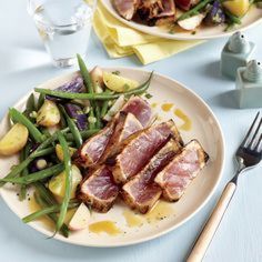 two plates with meat, green beans and potatoes next to a glass of water on a table