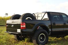 a black truck parked in the grass with two large tires on it's back