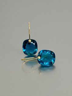 Elegant blue london topaz earrings featuring stunning brilliant drops. These faceted rectangular drops showcase a mesmerizing blue-green hue, imbuing the stones with remarkable depth and capturing and reflecting light beautifully. The fancy drops are skillfully attached to ear wires made of either 24K Gold Vermeil or 14K SOLID GOLD, adding a touch of luxury to these earrings. With their opulent appearance, these earrings make a bold and stylish statement. They are truly a magnificent pair of ear Luxury Timeless Topaz Jewelry, Luxury Blue Topaz Dangle Earrings, Elegant Blue Cushion Cut Earrings, Cushion Cut Gemstone Earrings For Gift, Modern Blue Earrings With Gemstone Accents, Modern Blue Topaz Earrings For Gift, Rock Crystal Jewelry, London Blue Topaz Earrings, Opal Drop Earrings