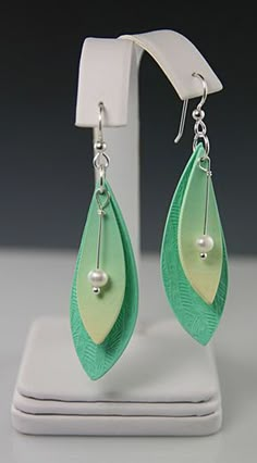 green and white earrings with pearls hanging from the earwires on a display stand