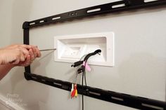 a person holding a pair of scissors in front of a wall mounted electrical outlet with wires attached to it