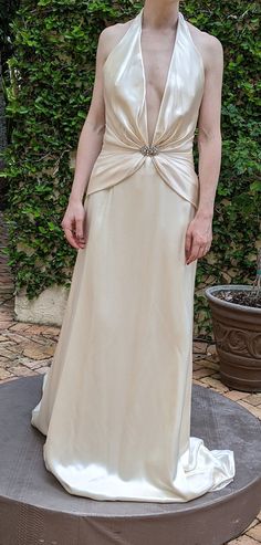 a woman in a white dress standing on top of a round object with bushes behind her