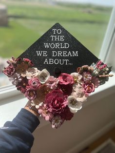 someone holding up a graduation cap that says to the world we dream about with flowers on it