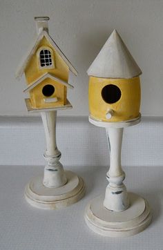 three ceramic birdhouses on pedestals with one yellow and the other white