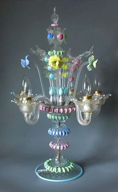 a glass chandelier with flowers and butterflies on it's sides, against a gray background