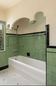 a bathroom with green tile walls and white bathtub next to a window in the corner