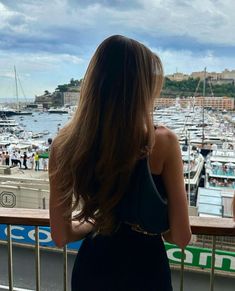 a woman in a black dress looking out over a harbor with boats on the water