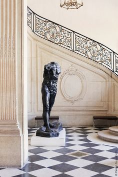 there is a statue in the middle of a room with stairs and chandelier