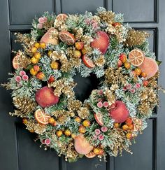 a wreath with oranges, pine cones and other decorations hanging on the front door