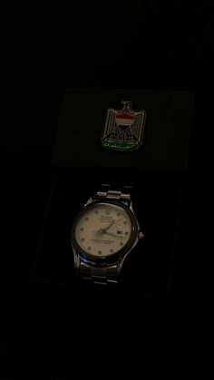 a watch sitting on top of a black box in the dark with an emblem behind it