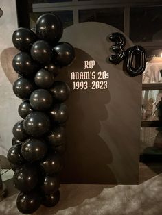 a bunch of black balloons sitting on top of a table in front of a sign