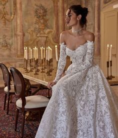 a woman in a white wedding dress sitting at a table with candles on the wall