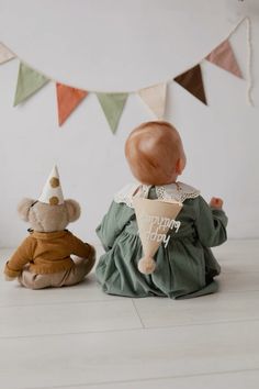 two stuffed animals sitting next to each other in front of a wall with bunting flags