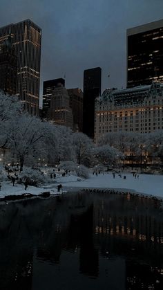 the city skyline is lit up at night with snow covered trees and buildings in the background