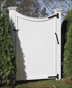 a large white gate in the middle of some bushes