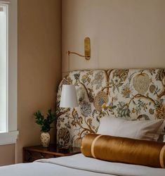 a bed with a floral headboard next to a window in a room that has pink walls and gold trim