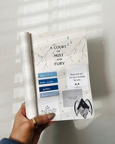 a person holding up a copy of the court of mist fury