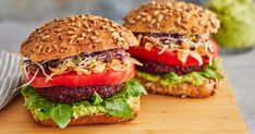 two hamburgers with lettuce, tomato and other toppings on a cutting board