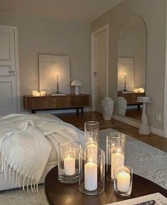 candles are placed on a table in front of a bed with white sheets and pillows