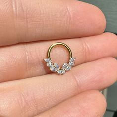 a person is holding a gold nose ring with three small stones on the top of it