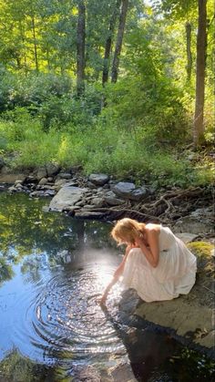 a woman in white dress sitting on rocks next to water