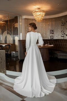 a woman in a white wedding dress looking at the back of her gown, with a chandelier hanging from the ceiling