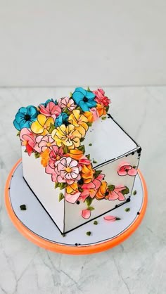 a cake decorated with flowers on an orange and white plate in the shape of a box