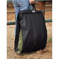 a man carrying a large black bag full of hay in front of a brown horse