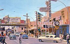 an old photo of cars and people walking on the street in front of buildings with neon signs