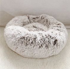 a round dog bed with furry fur on the top and bottom, in front of a white wall