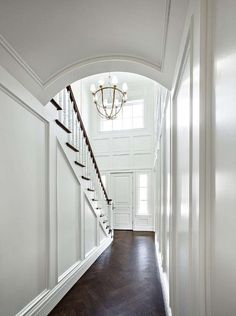 a hallway with white walls and wood flooring next to a chandelier hanging from the ceiling