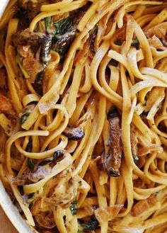 a white bowl filled with pasta and meat on top of a wooden table next to a fork