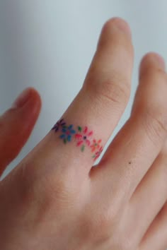 a person's hand with a small tattoo on it and colorful flowers in the middle