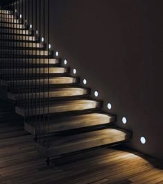 some lights that are on the side of a set of stairs in a room with wood flooring