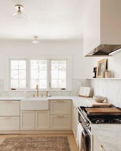 a kitchen with white cabinets and marble counter tops is pictured in this image, there are two windows above the sink