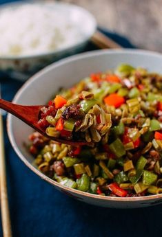 a white bowl filled with vegetables and rice next to chopsticks on a table