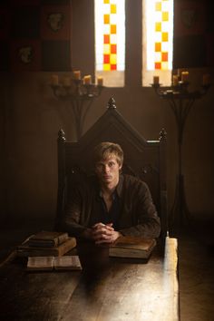 a man sitting at a table with books in front of him and two candles behind him