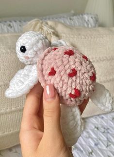 a hand holding a small crocheted turtle with hearts on it's shell