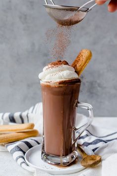 someone is sprinkling cinnamon on top of a hot chocolate drink with whipped cream