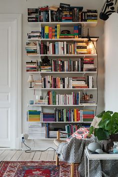 a bookshelf filled with lots of books next to a table and chair in a living room