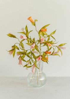 a glass vase filled with pink flowers on top of a white tableclothed surface