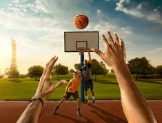 several people reaching for a basketball on a court with the sun setting in the background