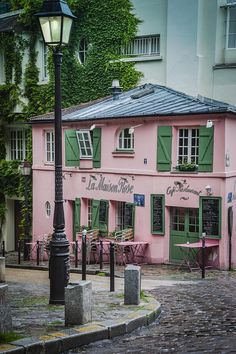 a pink building with green shutters on the windows and a lamp post in front