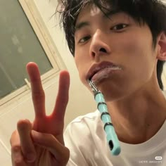 a young man is making the peace sign with his fingers and toothbrush in front of him