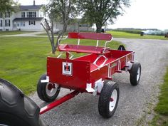 a red wagon sitting on top of a gravel road next to a green grass covered field