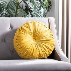 a yellow round pillow sitting on top of a gray couch next to a plant in a living room