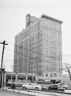 an old black and white photo of cars parked in front of a tall building