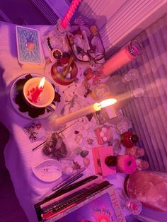 a table topped with lots of assorted items on top of a white bed covered in purple light