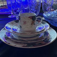 there is a cup and saucer on the table with blue glassware behind it