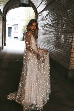 a woman is standing in an alley wearing a long white dress with stars on it